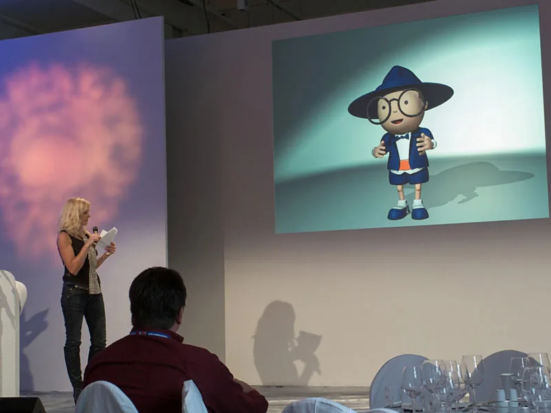 Digitales AutoScout24-Maskottchen Scouty auf einer Eventbühne neben einer Moderatorin